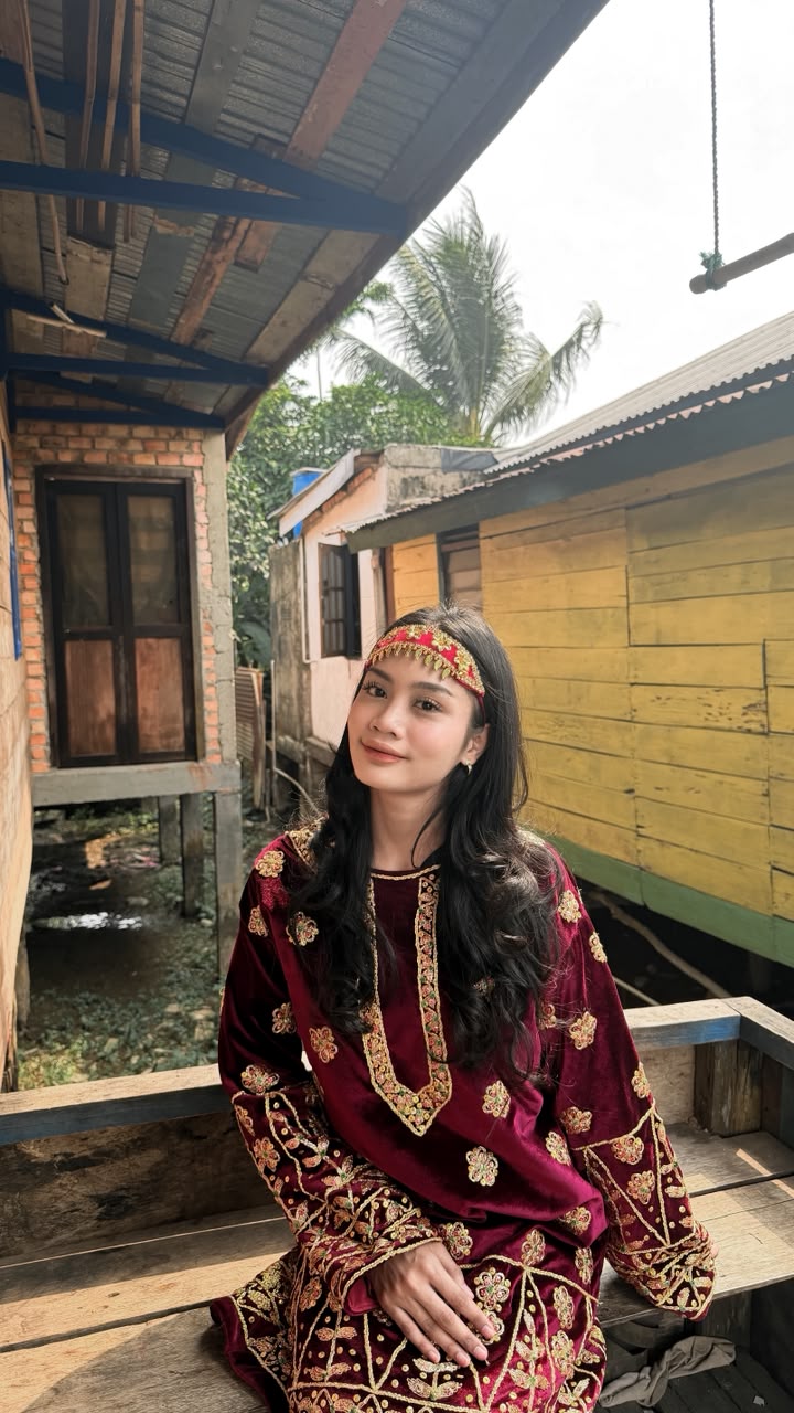 Balqis Putri Indira Duta Pariwisata Sumatera Selatan mengenakan busana beludru marun Sulam Angkinan asli di pelataran rumah panggung kayu khas Palembang
